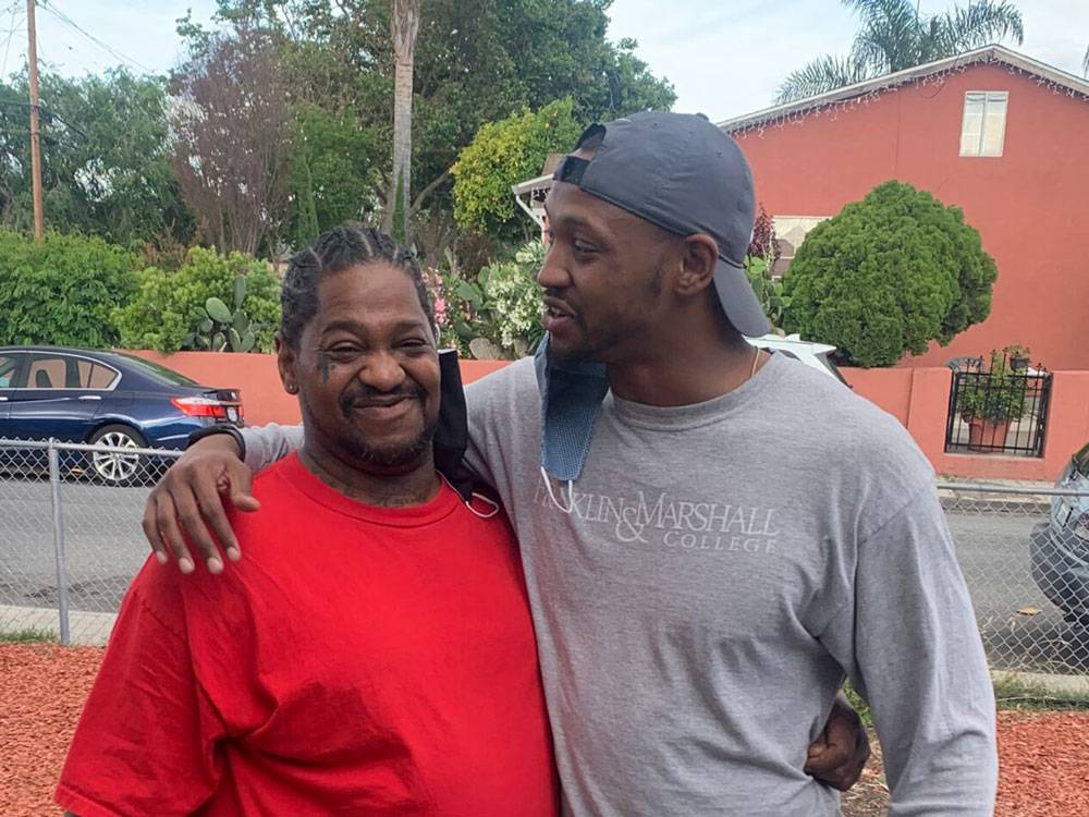 two men hugging out front of a home in a local East Palo Alto neighborhood