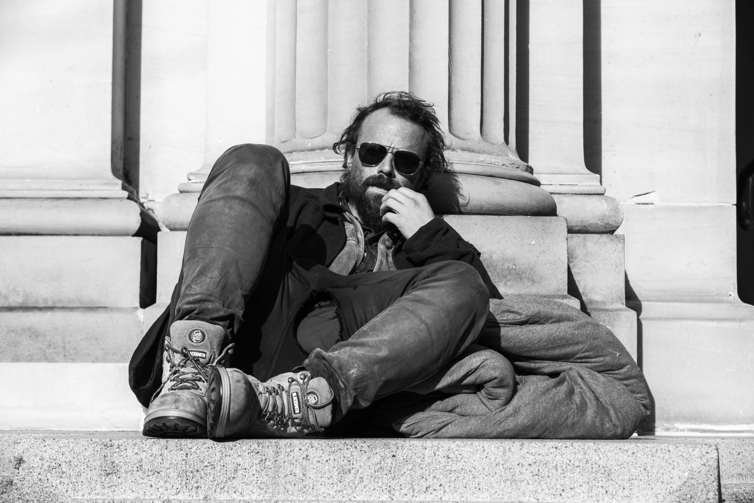 image of a man sitting on the ground leaning against a column with his backpack nearby