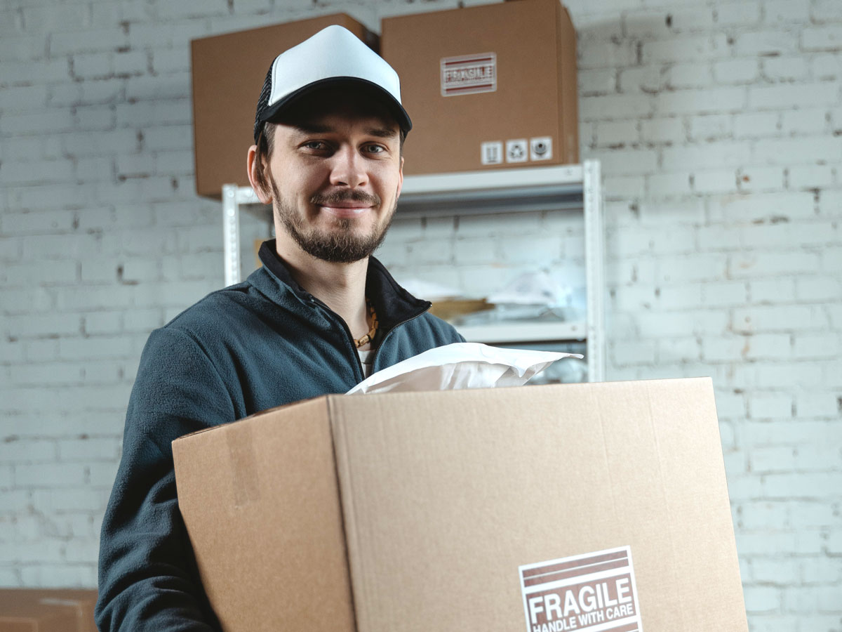 young man holding a box as if he is a mover or a delivery person