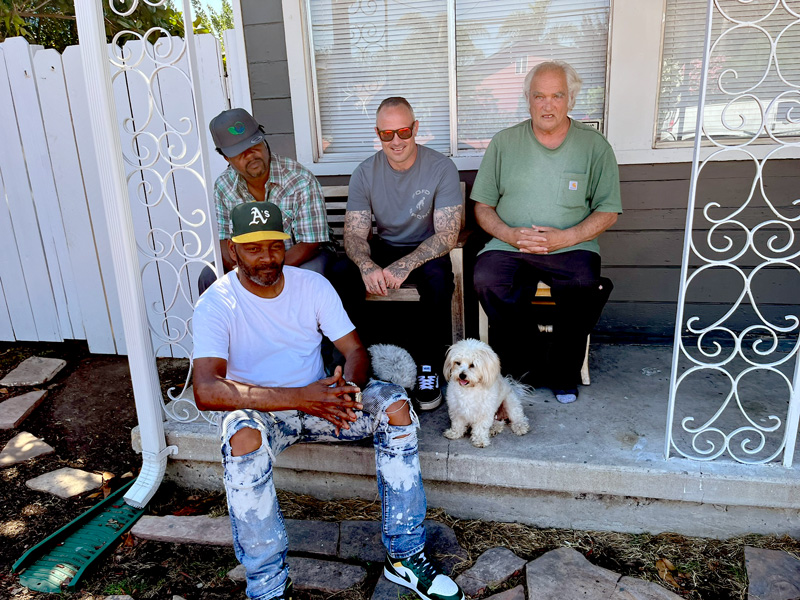 Retraining the Village men sitting on porch with dogs