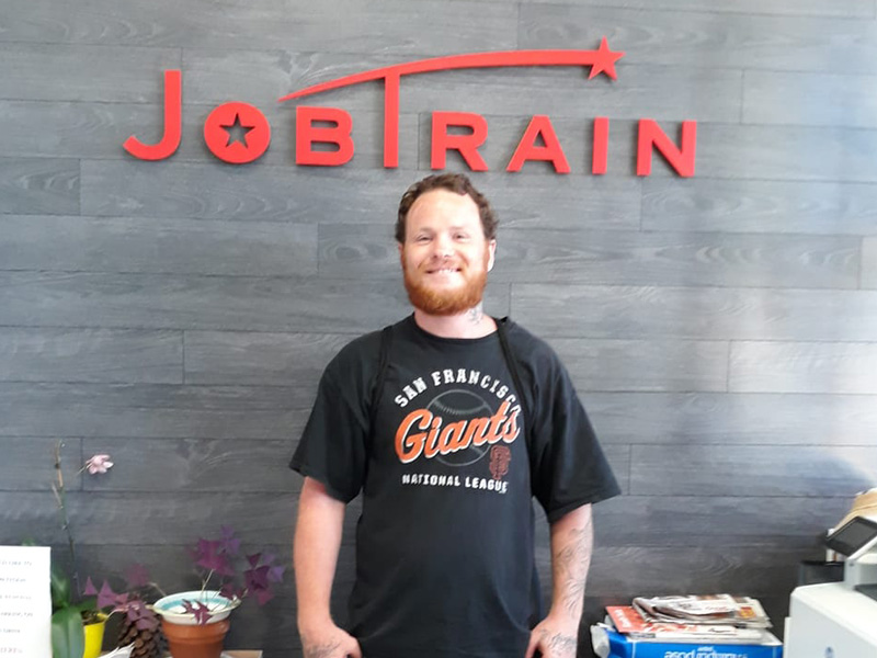 man smiling while standing under the JobTrain logo on a wall