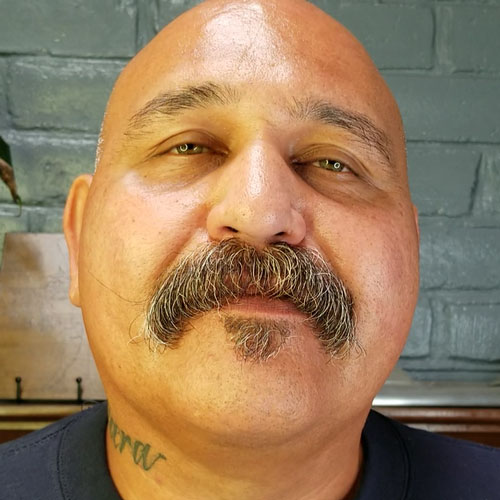 Luciano Beltran headshot, bald man with thick mustache and tattoo on neck