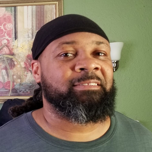 Quinn-Cory-Martin-Headshot Image of Quinn Cory Martin with black mustache and beard, wearing a green tshirt